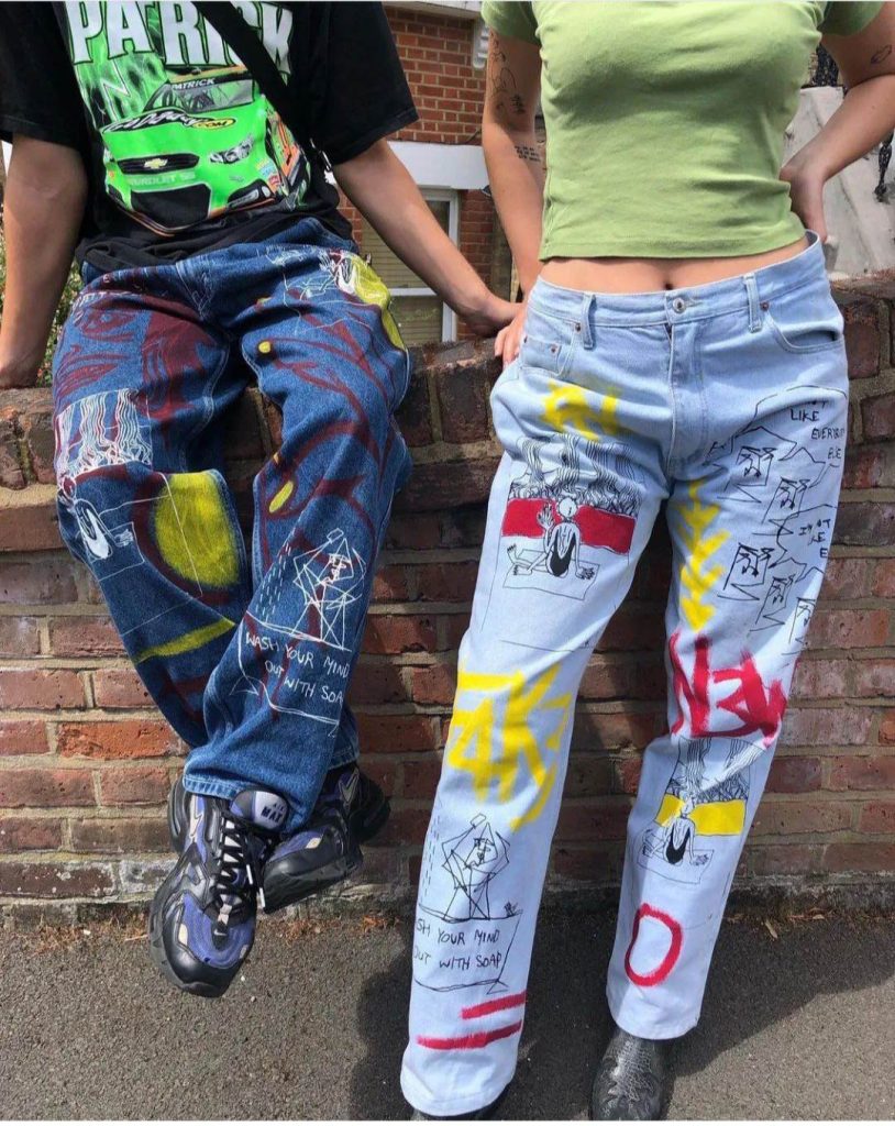 Cropped photo of two people wearing jeans with paintings on them.